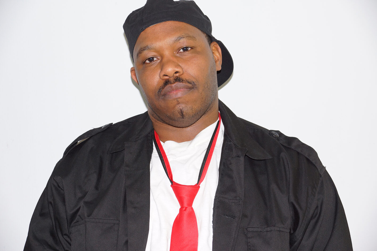 Chris Davios wearing a black military-style jacket with red tie, looking directly at the camera with confidence